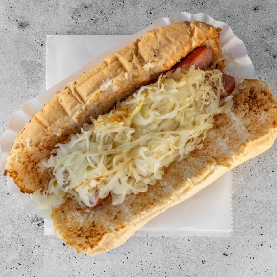 Top-down view of a hot dog with sauerkraut in a bun on a white paper tray.