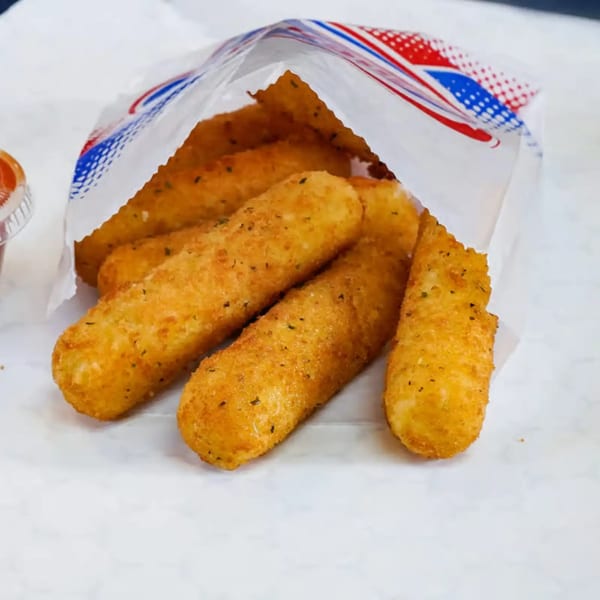 Golden-brown mozzarella sticks, seasoned with herbs, spilling out of a white paper bag with red and blue accents.