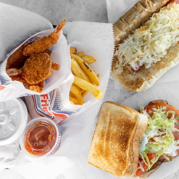 Fried shrimp, french fries, a hot dog with sauerkraut, and a sandwich with lettuce and tomato.