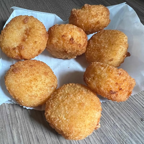 Seven golden-brown fried potato croquettes arranged on white parchment paper on a wooden surface.