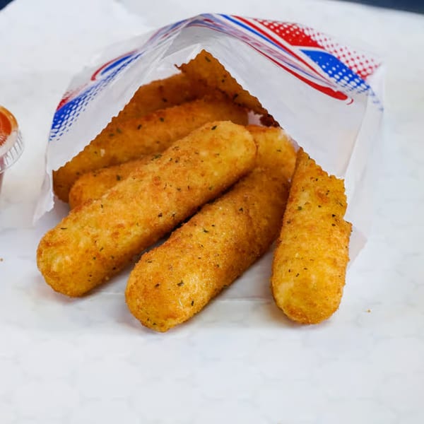 Golden-brown mozzarella sticks, seasoned with herbs, spilling out of a white paper bag with red and blue accents.