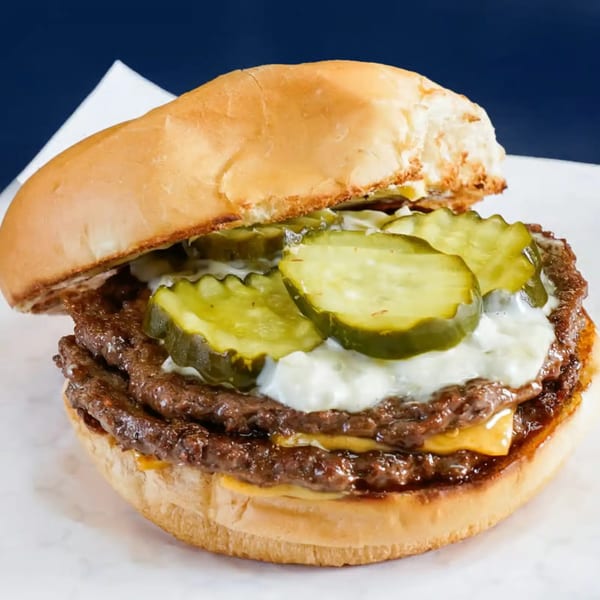 A double smash burger with melted cheese, pickles, and white sauce on a toasted bun.