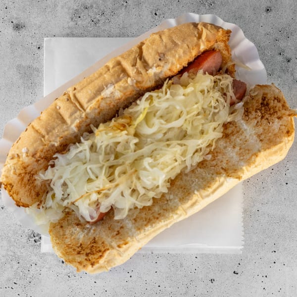 Hot dog with sauerkraut on a bun, served in a paper tray on a gray surface.