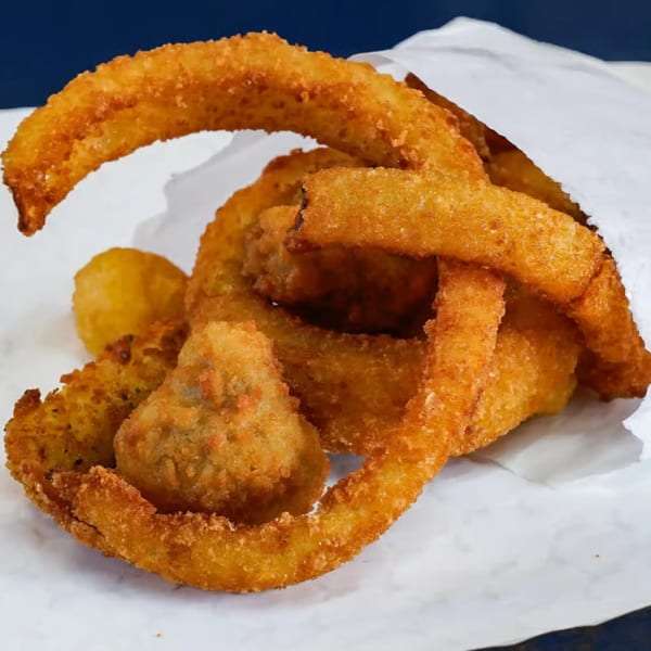 Crispy golden onion rings and fried mushrooms spilling from a white paper bag.