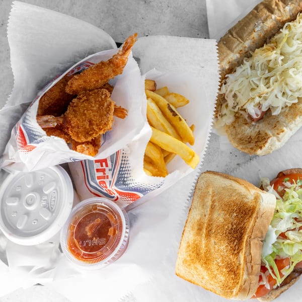 Fried shrimp, french fries, a hot dog with sauerkraut, and a sandwich with lettuce and tomato.